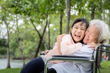 Granddaughter hugging grandmother in outdoor park,asian child girl hug senior woman are spending time together,elderly in wheelchair and child having laughing,smiling,enjoying,warm hands,care,support