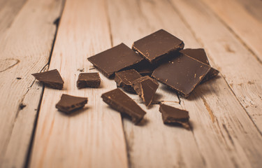 dark chocolate without sugar and gluten free for diabetics and allergics. Black chocolate broken into pieces lies in the center on a white table in a rustic style. Dark toning and vignette.