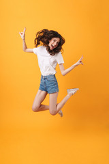 Fototapeta na wymiar Emotional happy young woman jumping isolated over yellow wall background showing peace.