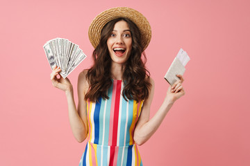 Positive shocked young cute woman posing isolated over pink wall background holding passport with tickets.