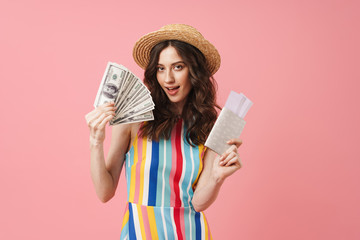Positive young cute woman posing isolated over pink wall background holding passport with tickets.