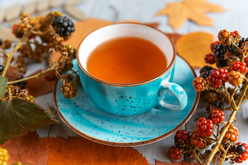 composition still life of a mug with hot leaf tea with berries and autumn leaves on a wooden surface
