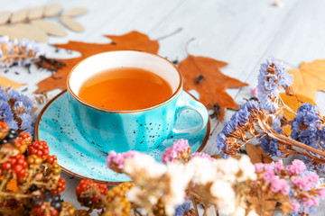 composition still life of a mug with hot leaf tea with berries and autumn leaves on a wooden surface