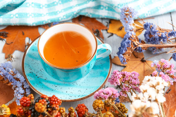 composition still life of a mug with hot leaf tea with berries and autumn leaves on a wooden surface