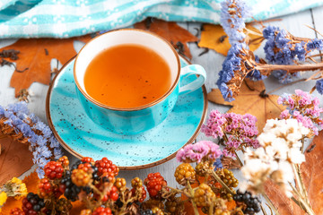 composition still life of a mug with hot leaf tea with berries and autumn leaves on a wooden surface