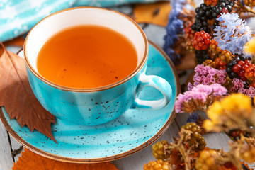 composition still life of a mug with hot leaf tea with berries and autumn leaves on a wooden surface