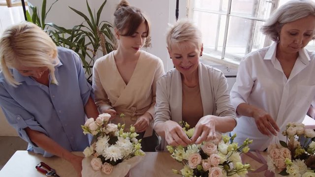 High angle view of Caucasian women standing at worktop and arranging flowers into compositions during master class in art studio