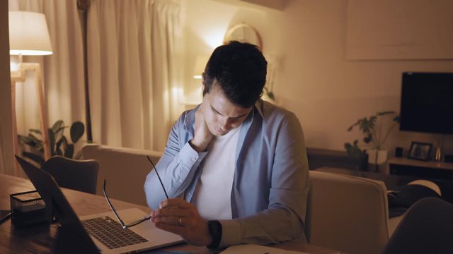 Tired man suffering from neck pain working till late night on laptop