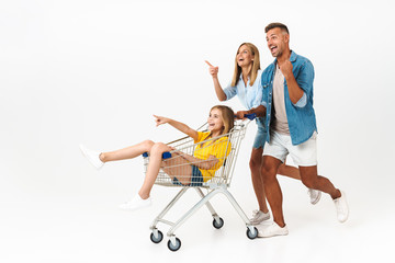 Image of happy family man and woman having fun while giving ride to their daughter in shopping cart