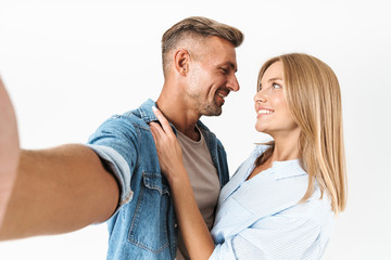 Portrait of excited caucasian couple man and woman in basic clothing smiling and taking selfie photo together