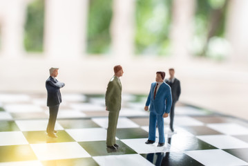 Business strategy. Miniature businessman standing on chessboard with chess pieces.