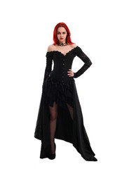 Fototapeta premium full length portrait of a red haired girl wearing a black gothic gown, Standing pose on a grey studio background.