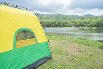 Camping green-yellow tent in forest near lake.