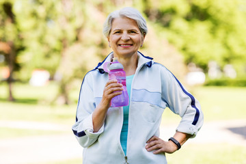 fitness, sport and healthy lifestyle concept - happy smiling sporty senior woman with bottle of water at summer park