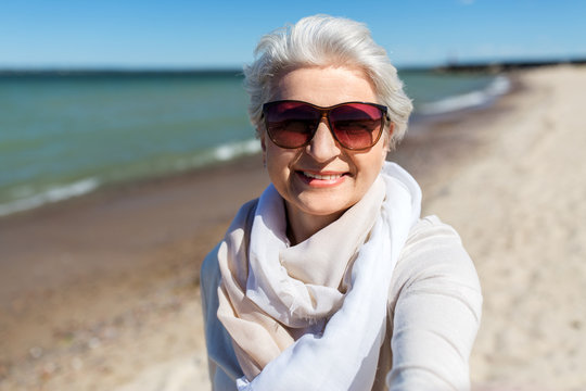 old people and leisure concept - happy smiling senior woman in sunglasses taking selfie on beach in estonia