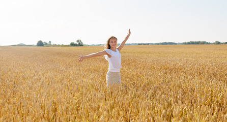 nature, harvest and freedom concept - happy young girl with hands outstretched on cereal field in summer