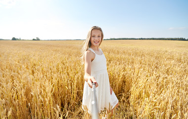 technology, summer and people concept - happy young girl in white dress taking picture by selfie stick on cereal field