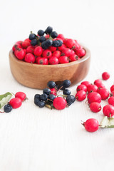 Fresh hawthorn berries (thornapple, May-tree, whitethorn, hawberry) in the wooden small bowl on the white table. Herbal medicine. Selective focus.