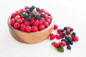 Fresh hawthorn berries (thornapple, May-tree, whitethorn, hawberry) in the wooden small bowl on the white table. Herbal medicine. Selective focus.