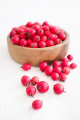 Fresh hawthorn berries (thornapple, May-tree, whitethorn, hawberry) in the wooden small bowl on the white table. Herbal medicine. Selective focus.