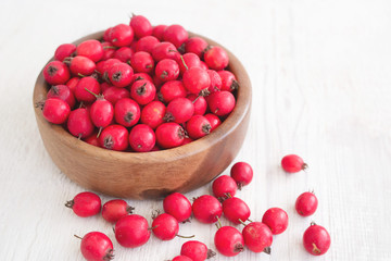 Fresh hawthorn berries (thornapple, May-tree, whitethorn, hawberry) in the wooden small bowl on the white table. Herbal medicine. Selective focus.