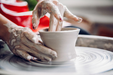 Young woman in red apron works behind potter wheel with length, making handmade plate. Concept of concentration, creativity hand