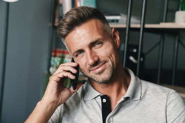 Photo closeup of beautiful caucasian man talking on smartphone while resting at home