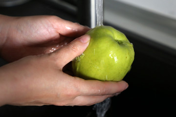 Woman washes a green apple under tap water. Concept of hygiene, clean fruit in female hands