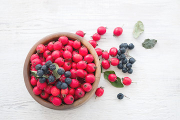 Fresh hawthorn berries (thornapple, May-tree, whitethorn, hawberry) in the wooden small bowl on the white table. Herbal medicine. Selective focus.