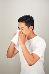 Closeup of sick Asian man blowing nose into tissue, suffering from common cold. Medical and healthcare concept on white background
