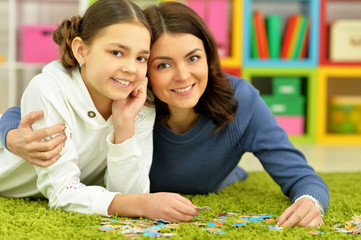 Fototapeta premium Portrait of mother with little daughter collecting puzzles