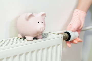 oman inspecting warming of heating radiator near piggy bank.Energy saving concept