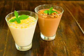 Dessert chocolate pudding with nuts and vanilla pudding with lemon zest on a wooden table.