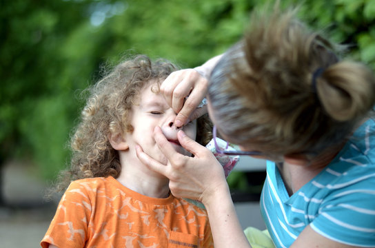 Mama macht die Nase ihres Kindes sauber während das Kind protestiert