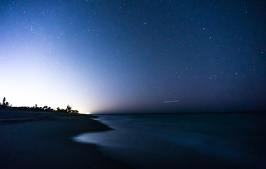 Light pollution lights up a star filled night at Hobe Sound Beach, looking north as a plane dots the sky, Jupiter Island, Martin County, Florida, USA