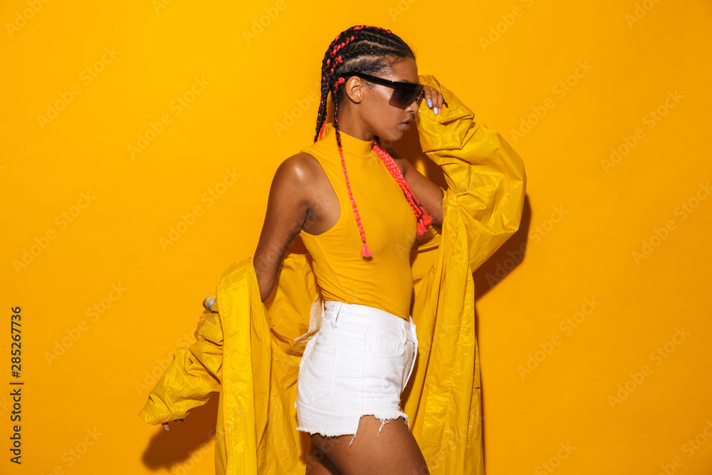 Wall mural Image of alluring african american woman wearing sunglasses and windcoat posing at camera