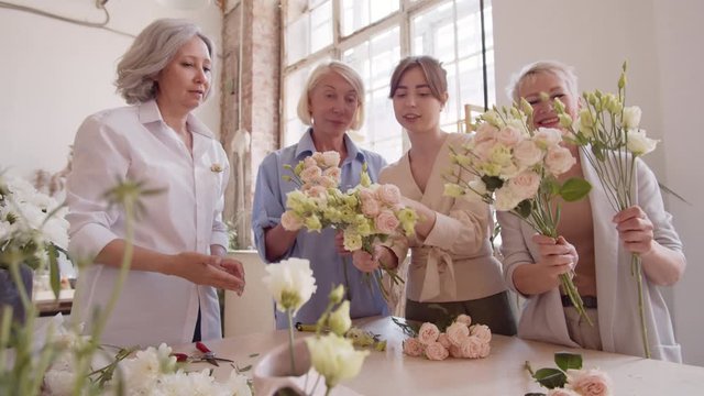 Panning of young female florist and three middle-aged female students making bouquet together in florist workshop
