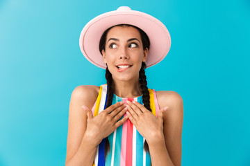 Image of modest brunette girl wearing summer dress and hat looking aside at copyspace