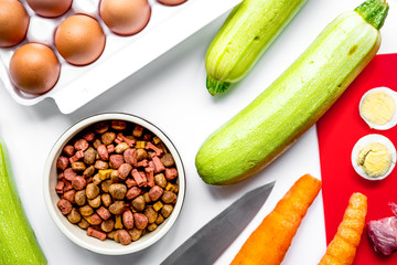 Bowl of dry dogfood, carrot, courgette and meat table background top view