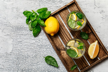 Obraz na płótnie Canvas Summer basil lemonade on grey background. Fresh summer cocktail with basil, lemon and ice cubes. Homemade fresh lemonade with lemon and basil. Food and drink concept