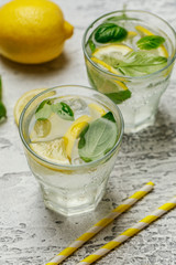 Summer basil lemonade on grey background. Fresh summer cocktail with basil, lemon and ice cubes. Homemade fresh lemonade with lemon and basil. Food and drink concept