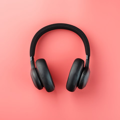Wireless black headphones on a pink background. View from above. In-ear headphones for playing games and listening to music tracks.