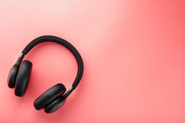 Wireless black headphones on a pink background. View from above. In-ear headphones for playing games and listening to music tracks.