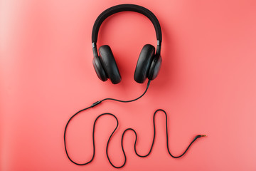 Black headphones on a pink background. Sound frequency made from earphone wire. In-ear headphones for playing games and listening to music tracks