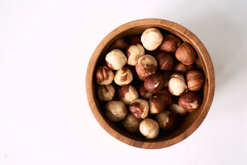 Hazelnut in brown bowl on textured wooden background, top view.