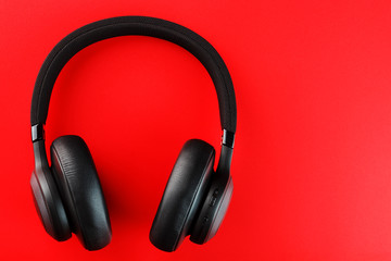 Wireless black headphones on a red background. View from above. In-ear headphones for playing games and listening to music tracks
