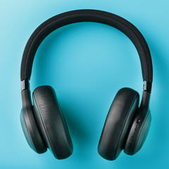 Wireless black headphones on a blue background. View from above. In-ear headphones for playing games and listening to music tracks