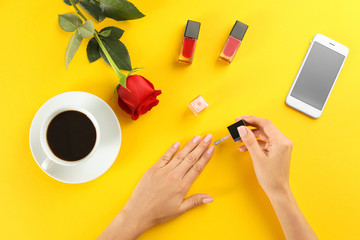 Woman applying nail polish on color background, top view