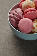 Blue bowl with tasty pink and white macaroons and pink zephyr on gray background