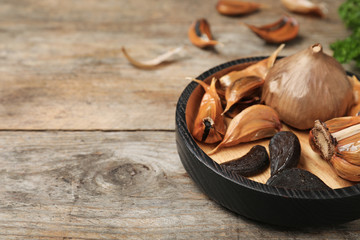Bowl with black garlic on wooden table. Space for text